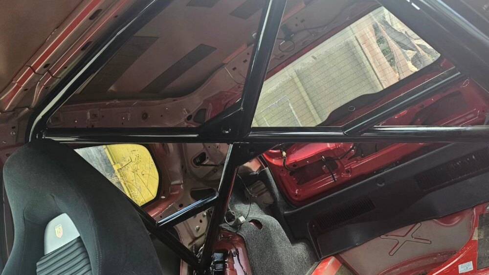 A black JP Cages half cage fitted behind the front seats of a stripped red Fiat Punto Mk3