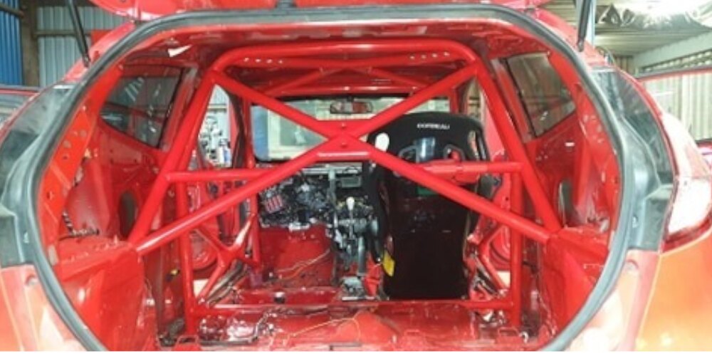 A red JP Cages multipoint roll cage with X bracing in a stripped red Ford Fiesta MK7, seen through the tailgate
