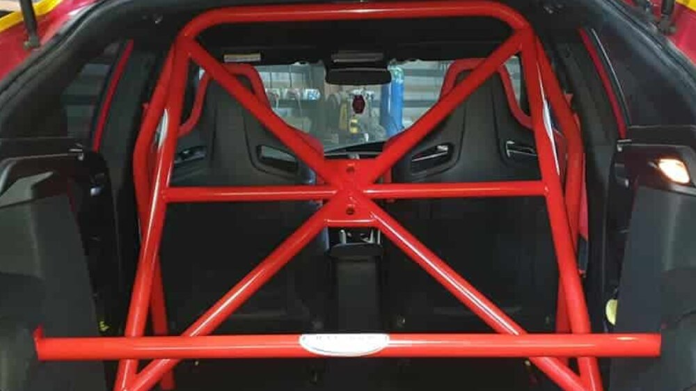 A red JP Cages half cage with X bracing and a harness bar behind the front seats of a red Honda Civic FK2, seen through the tailgate