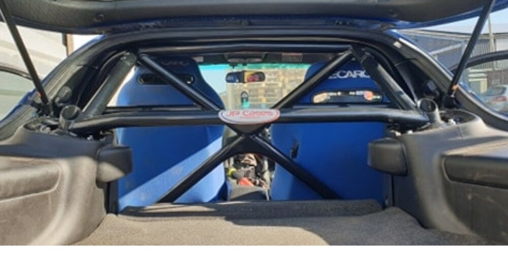 A black JP Cages half cage with X bracing seen through the open hatch of a blue Mazda RX-7 FD
