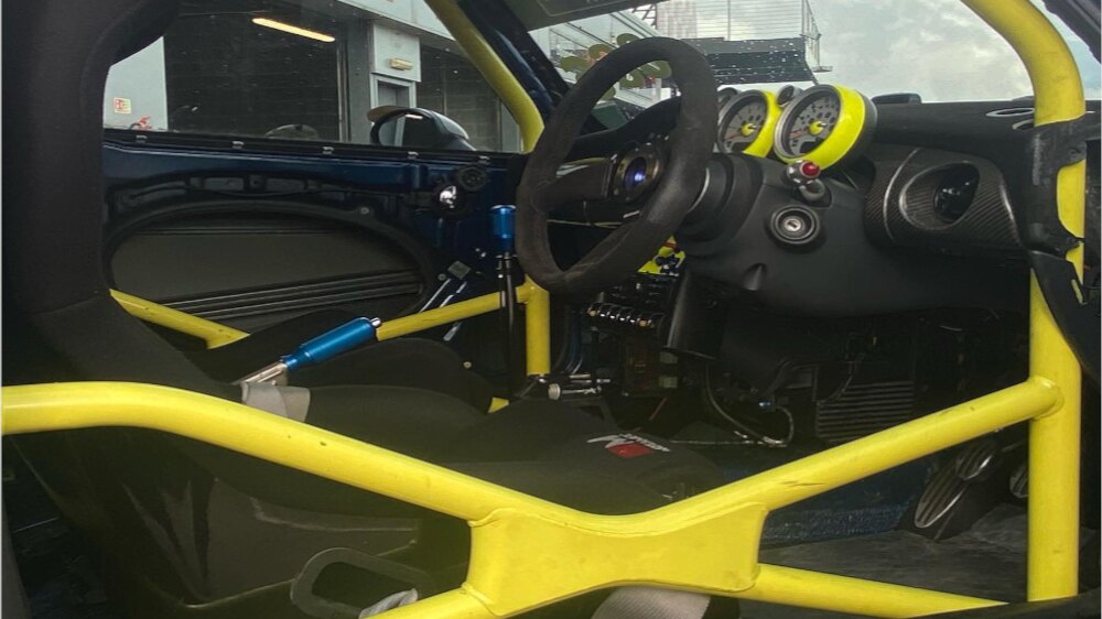 A yellow JP multipoint roll cage with door bars inside a blue Mini, seen through the open driver's door