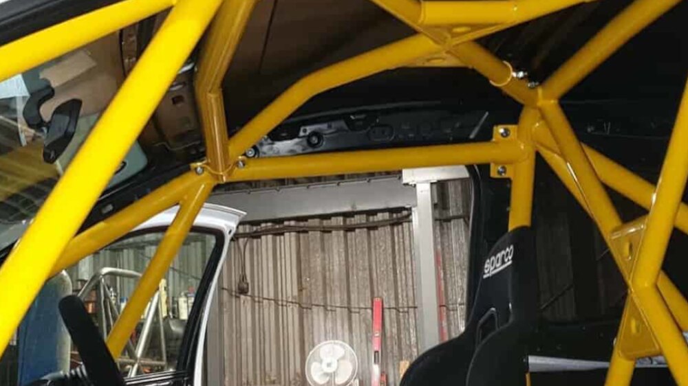 A yellow JP Cages multipoint competition cage with door bars and roof bracing inside a Renault Clio MK3, with a black Sparco bucket seat fitted