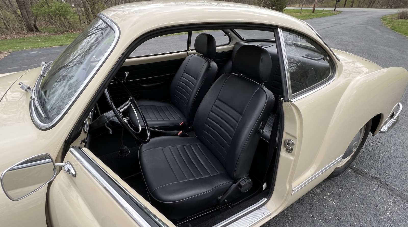 Cream 1970 Volkswagen Karmann Ghia with the driver door open showing a black classic style reclining bucket seat, its runners and recline handwheel visible above the floor