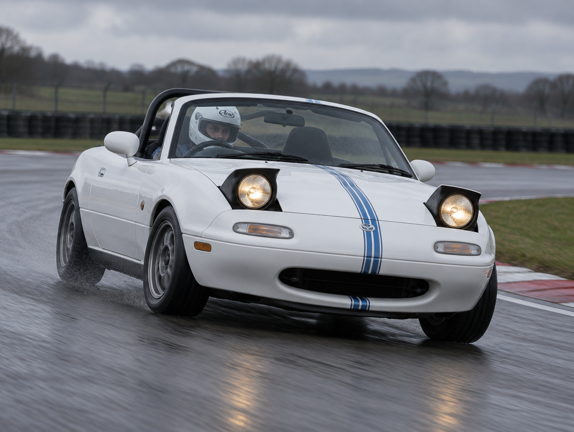 White Mazda MX-5 Mk1 NA with a helmeted driver cornering on a wet British circuit