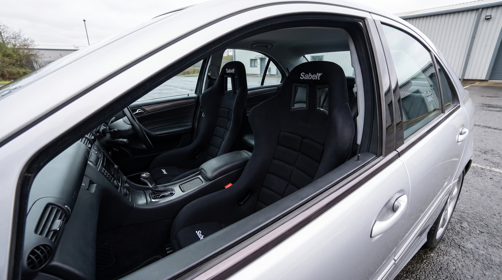Pair of black Sabelt GT3 fixed back FIA bucket seats fitted in a silver Mercedes-Benz C32 AMG W203 saloon, the Sabelt name across the top of each backrest, seen over the open driver door window