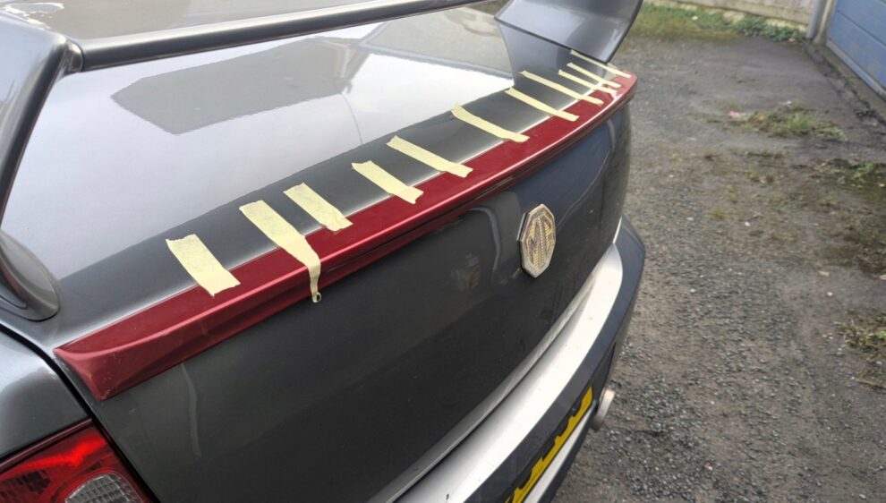 A boot lip spoiler taped and clamped in position on the MG ZS boot lid during test fitting