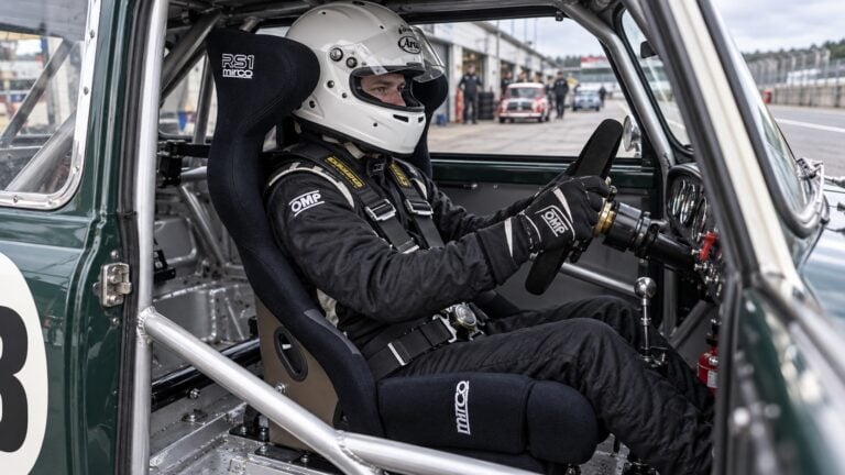 Helmeted Mini Miglia driver in a black Mirco RS1 FIA racing seat inside a caged classic Mini