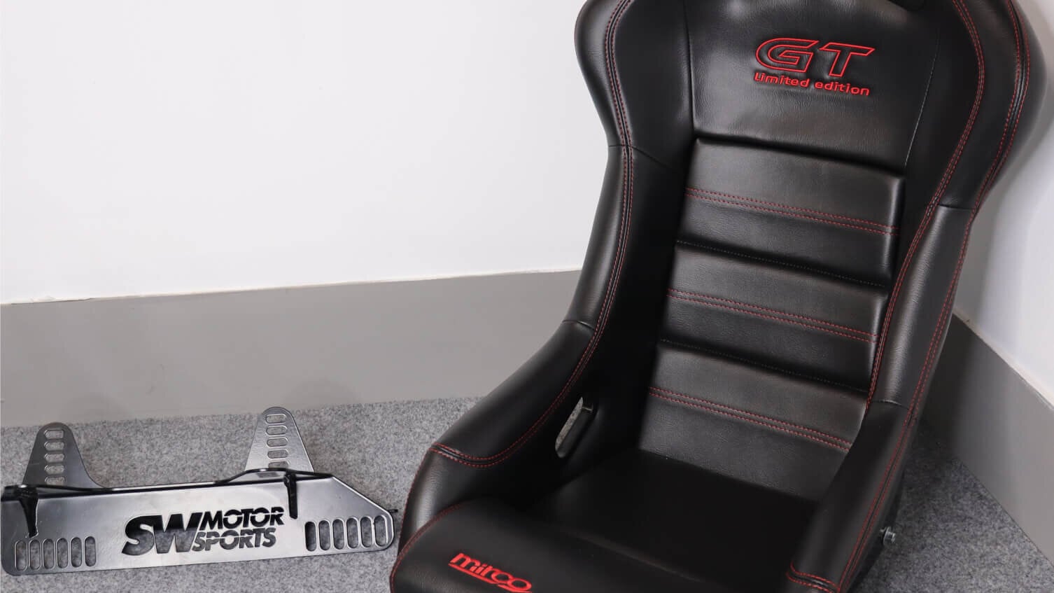 A black vinyl Mirco GT Limited Edition bucket seat with red stitching beside an SW Motorsports side mount on the GSM Performance showroom floor