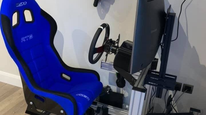 A blue Mirco RTS bucket seat on a customer's aluminium sim racing rig with a wheel and a curved monitor