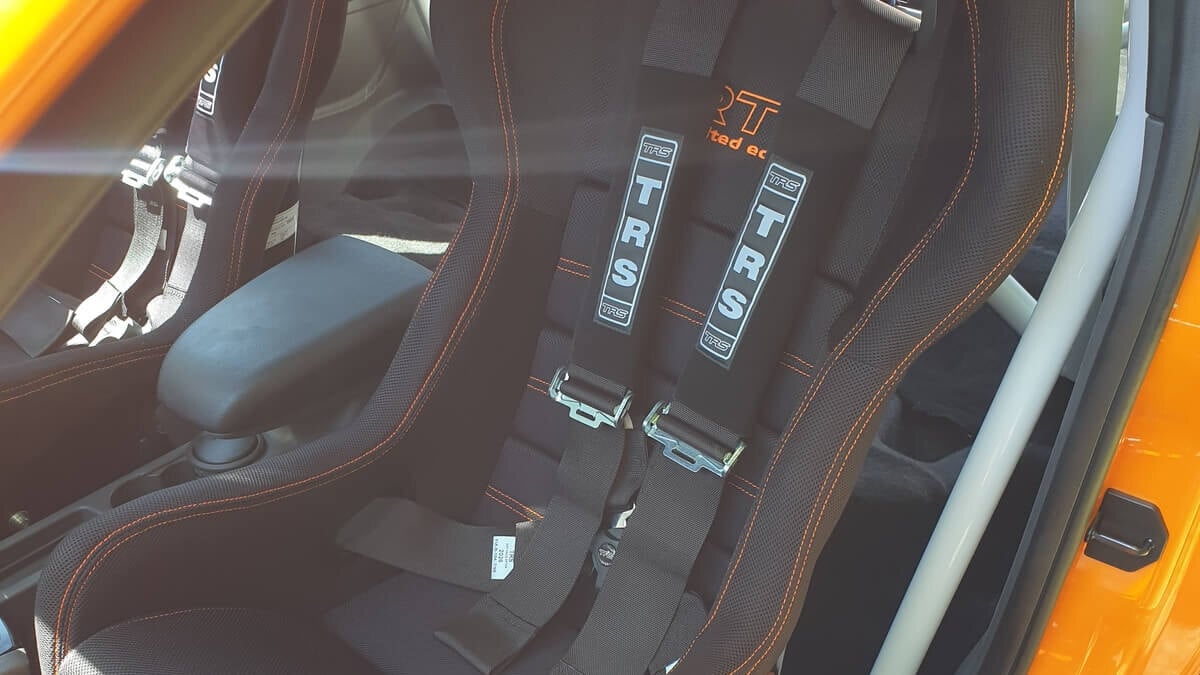 A black Mirco RTS bucket seat with orange stitching and a black TRS harness in an orange Ford Focus ST with a white roll cage