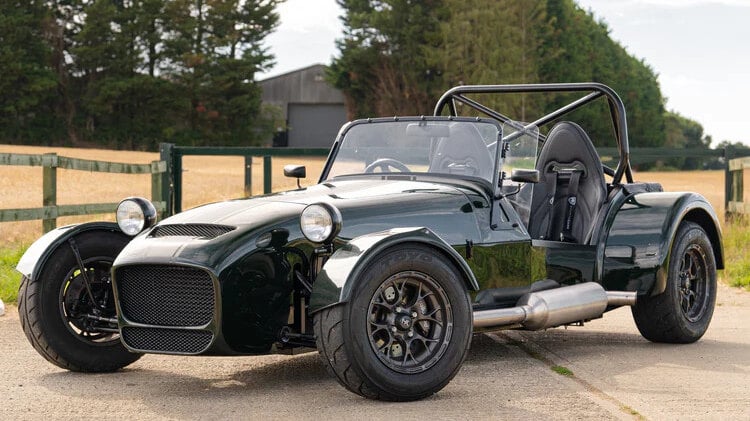 A dark green MK RX-5 kit car with a roll bar and black bucket seats, parked on a concrete yard