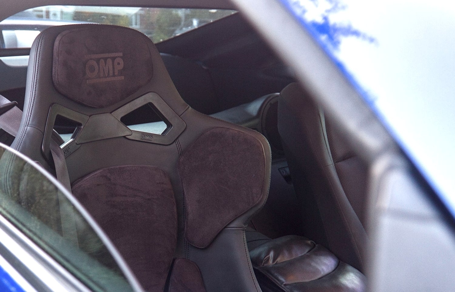 An OMP RT fibreglass FIA bucket seat in black with alcantara and leather pads, fitted to a blue Nissan 350Z on an M2 Motorsport direct fit sub-frame, with the factory leather seat still in place alongside it
