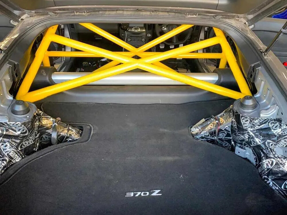 A yellow bolt-in half roll cage fitted in a Nissan 370Z, seen through the open tailgate