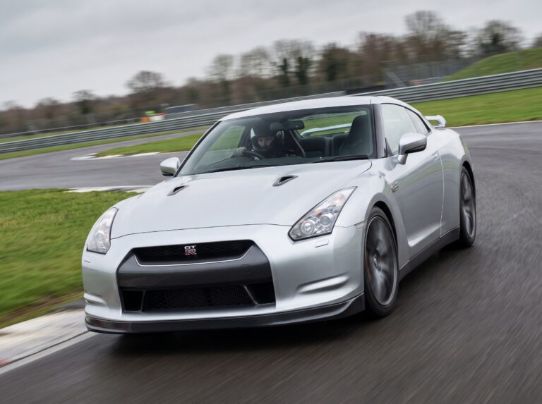 Silver Nissan GT-R R35 cornering on a British race circuit with helmeted driver at the wheel