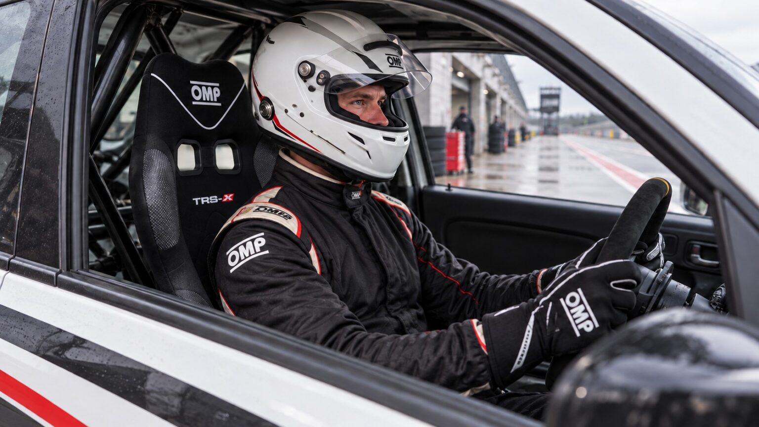 Helmeted driver checking the fit of an OMP TRS-X narrow racing seat in a stationary track car