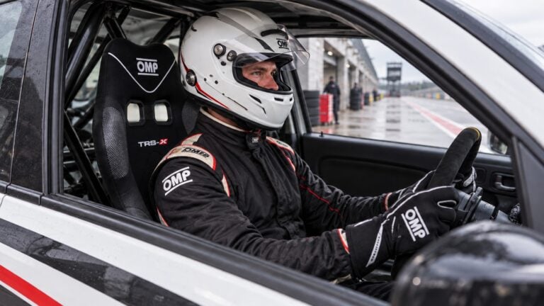 Helmeted driver checking the fit of an OMP TRS-X narrow racing seat in a stationary track car