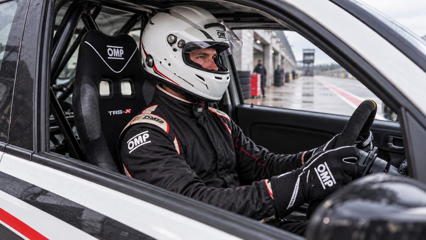 Helmeted driver checking the fit of an OMP TRS-X narrow racing seat in a stationary track car