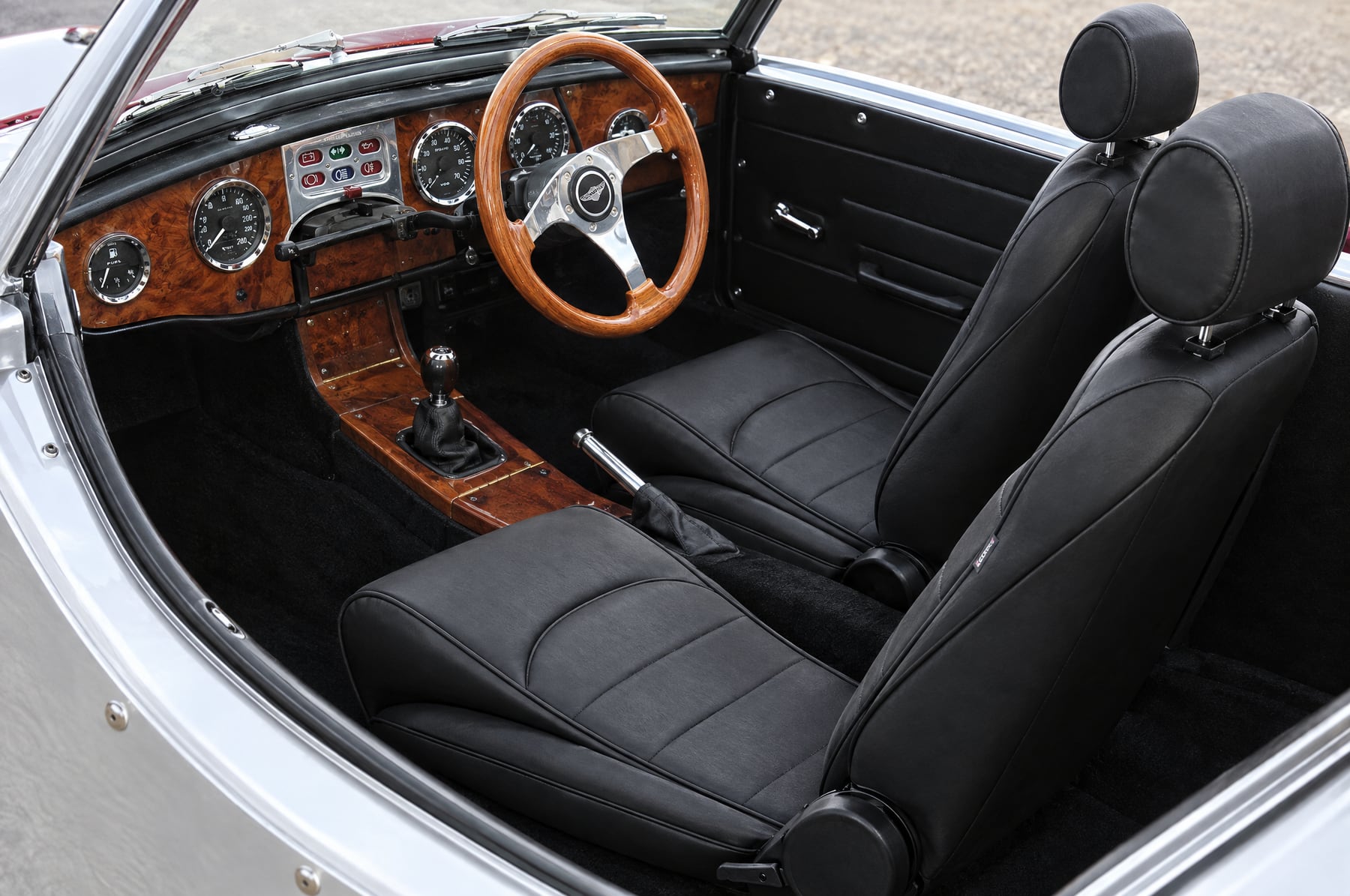 Cockpit of a right hand drive Panther Kallista with a walnut dash and a pair of black Corbeau Sportsman reclining seats