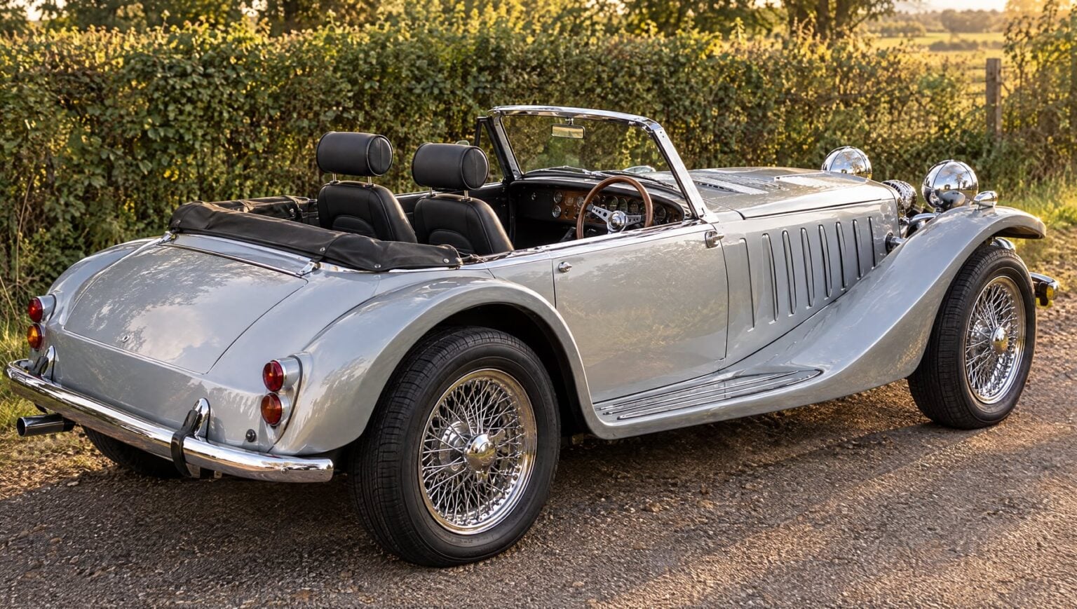 Rear three quarter view of a silver Panther Kallista showing the Corbeau Sportsman seats and headrests above the folded hood