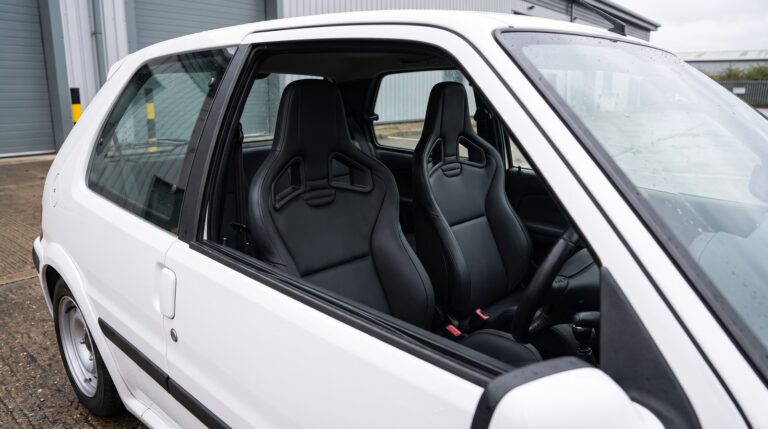 Pair of black Recaro Sportster CS reclining sport seats fitted in a white Peugeot 106, seen through the open driver door window