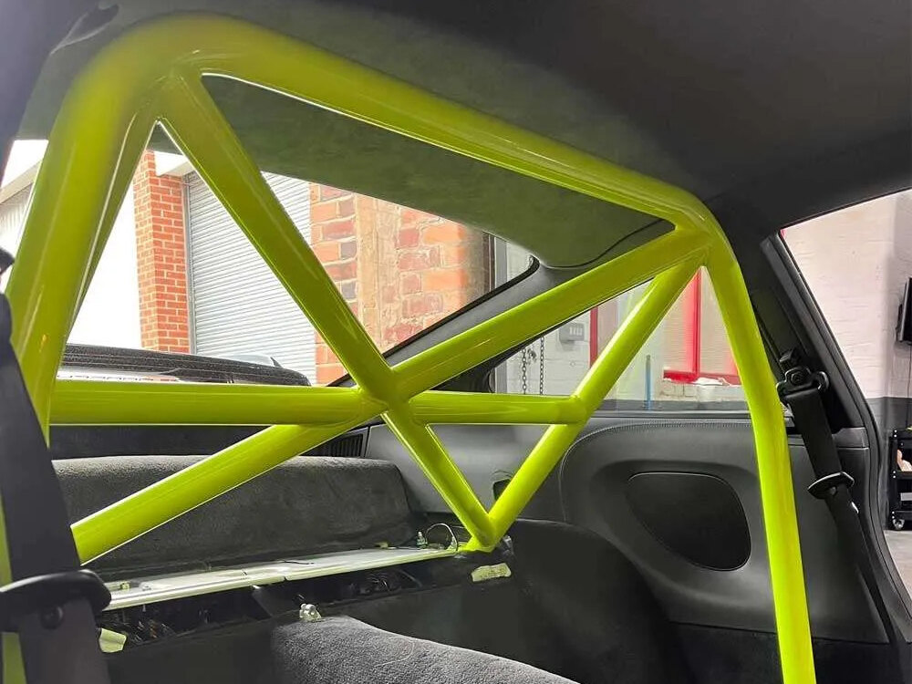 A fluorescent green bolt-in half roll cage behind the seats of a Porsche coupe