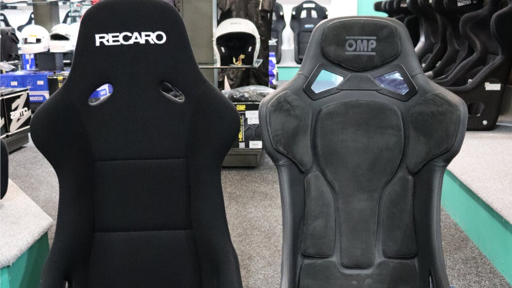 A black Recaro Pole Position ABE and a black OMP RT bucket seat side by side on the showroom floor