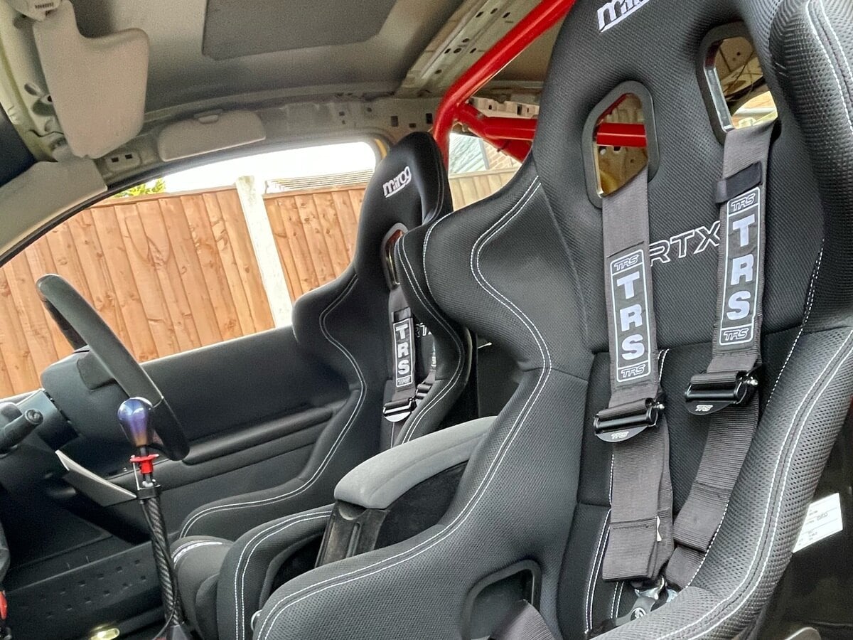 A pair of black Mirco RTX-7 bucket seats with grey TRS harness straps fitted in a customer's Renault Megane track car, with a red roll cage behind