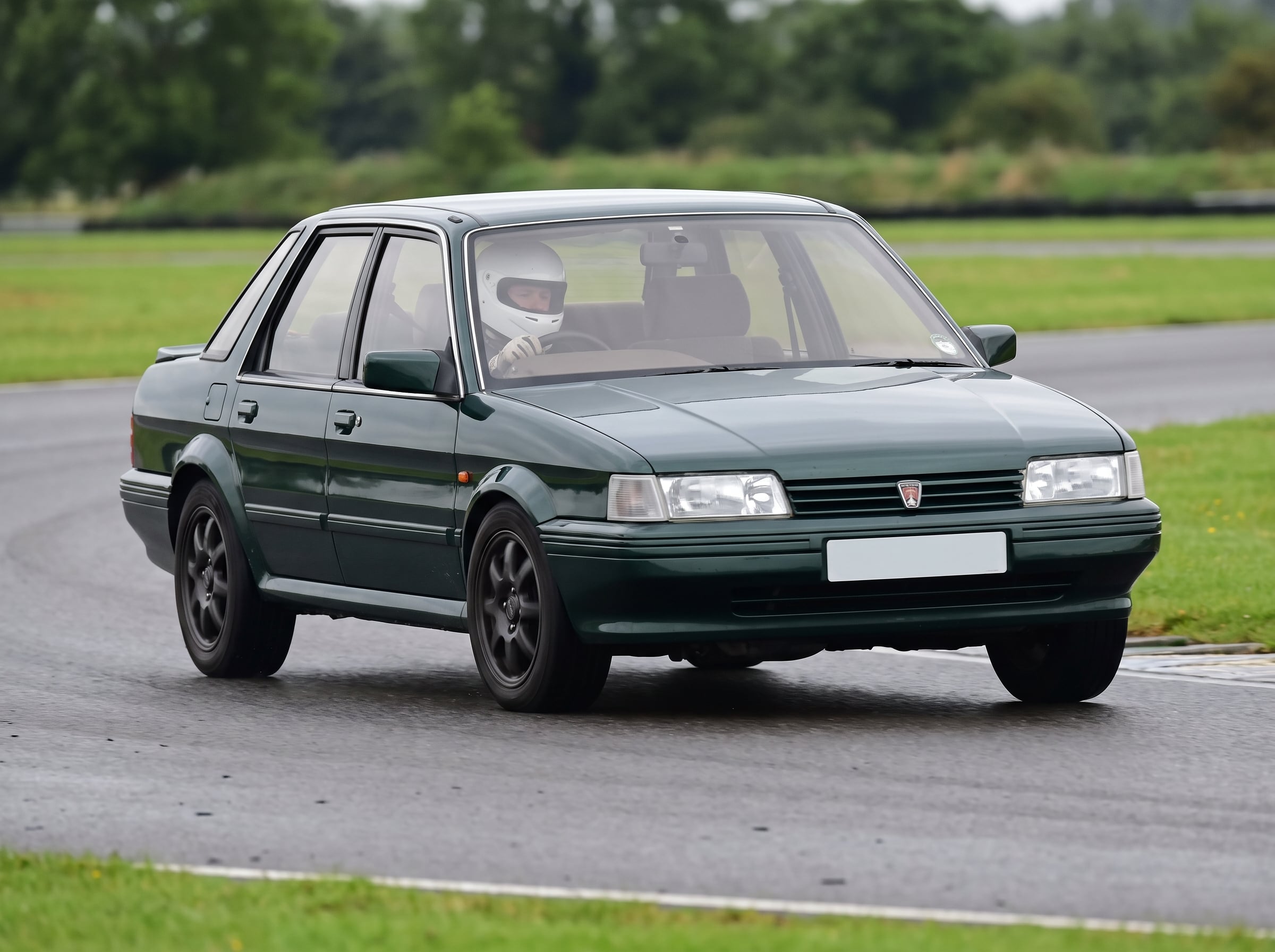 Dark green Rover Montego saloon on a British race circuit, driver in white helmet visible through the windscreen