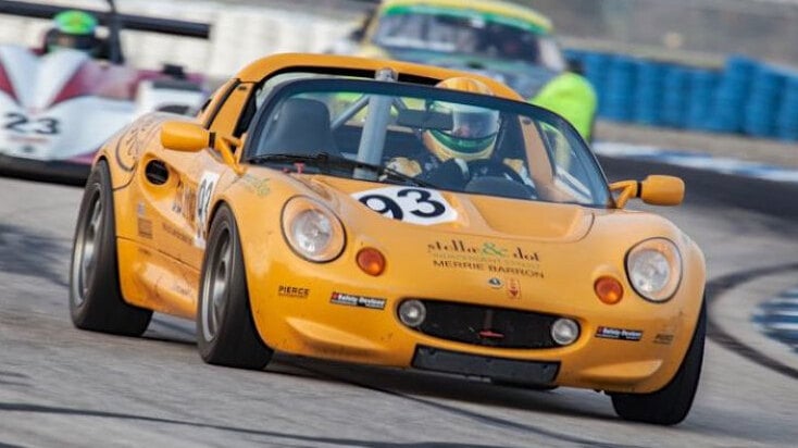 A yellow Lotus Elise race car with a roll cage and Safety Devices decals cornering on a circuit