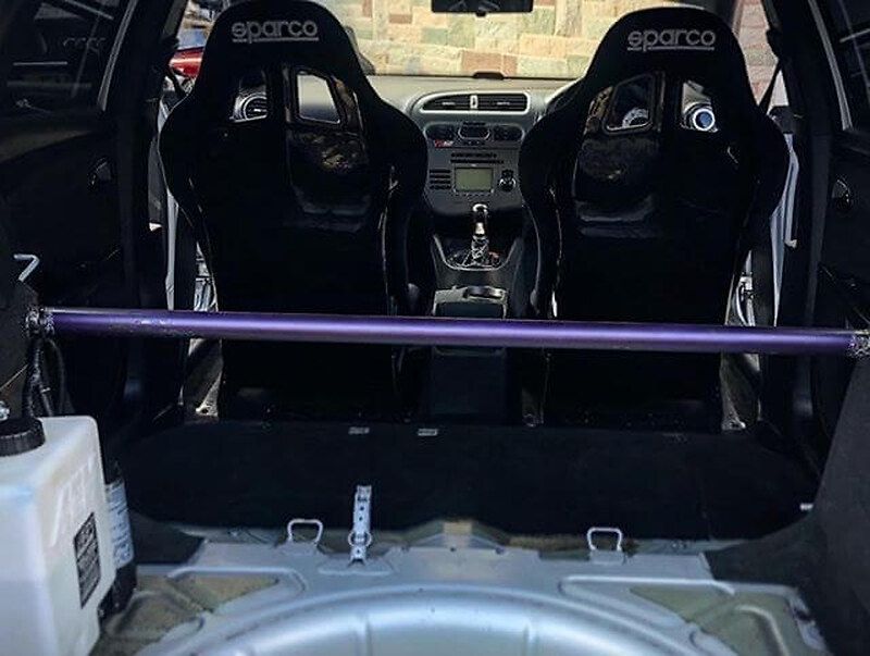 Two black Sparco Rev QRT bucket seats seen through the open boot of a Seat Leon Cupra, with a purple bar across the car behind them
