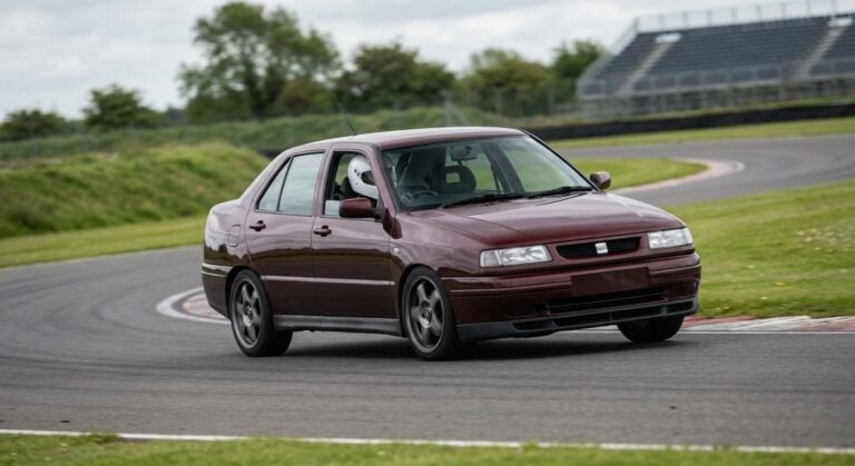 Dark red Seat Toledo Mk1 cornering on a British race circuit with a helmeted driver visible through the windscreen