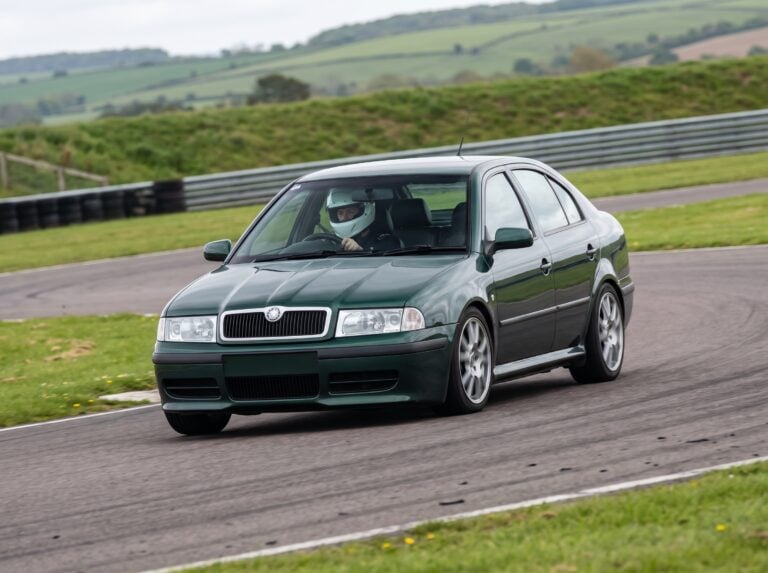 Skoda Octavia Mk1 hatchback cornering on a British race circuit with a helmeted driver visible through the windscreen