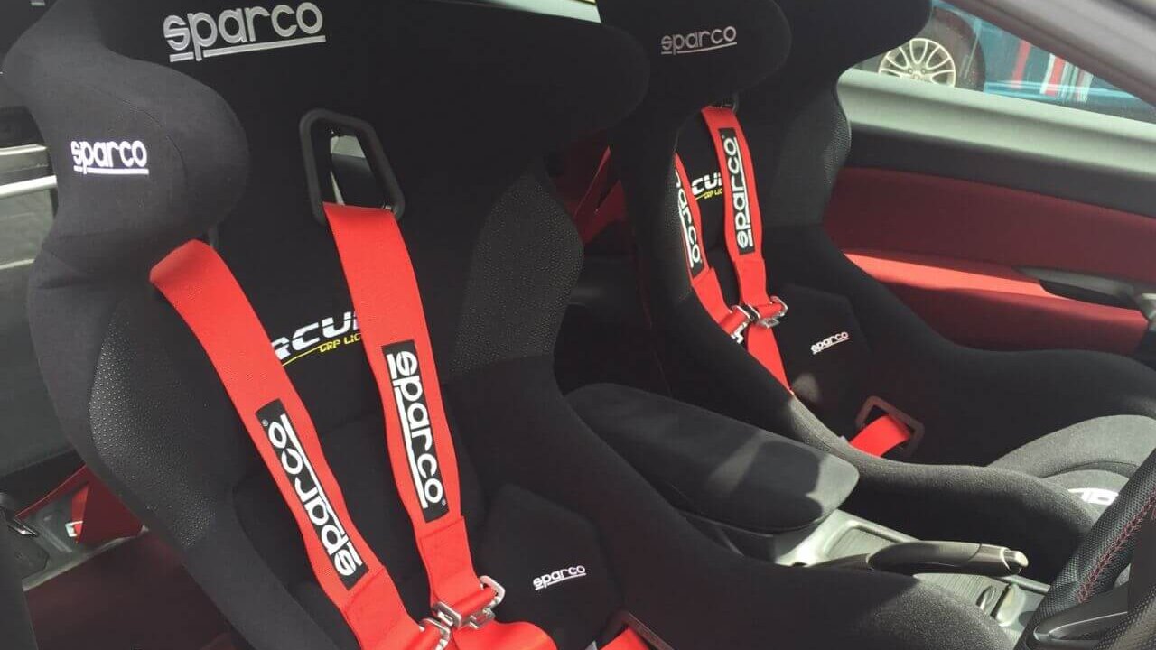 Two black Sparco bucket seats with red Sparco harnesses fitted in a car