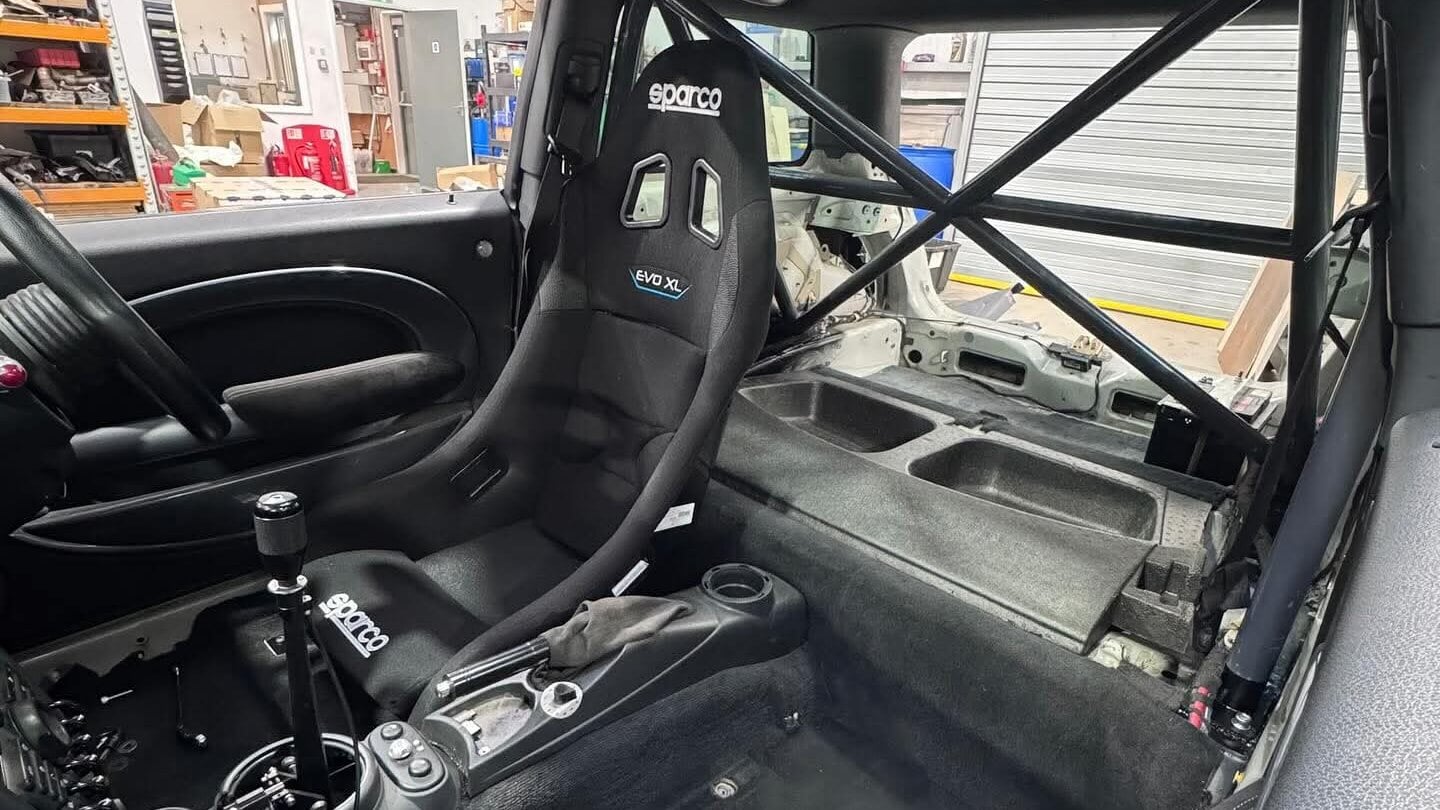 A black Sparco Evo XL bucket seat fitted on the driver side of a customer's Mini R53, with the door card, carpet and a roll cage in view