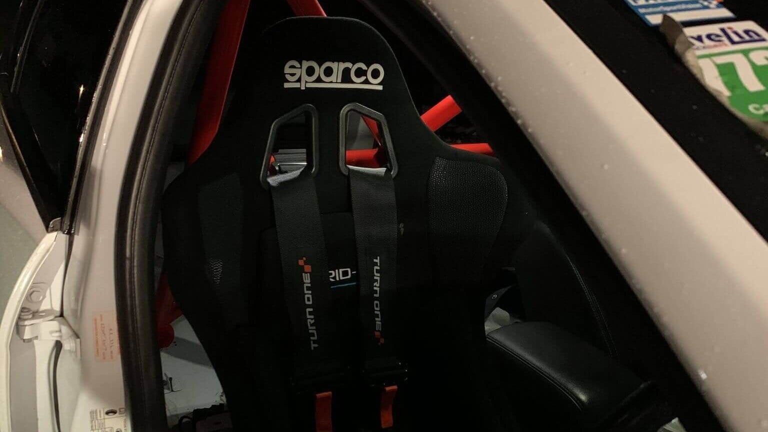 A black Sparco Grid-Q bucket seat with a harness fitted in a white race car with a red roll cage