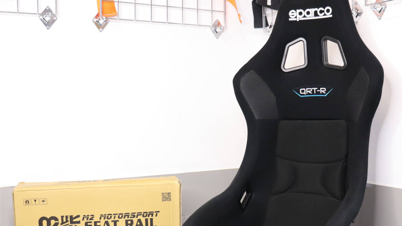 A black Sparco QRT-R bucket seat beside a boxed M2 Motorsport seat rail in front of the harness display in the GSM Performance showroom
