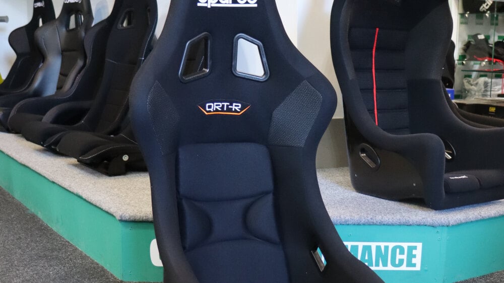 A black Sparco QRT-R sim racing seat on the showroom floor in front of the seat display plinth