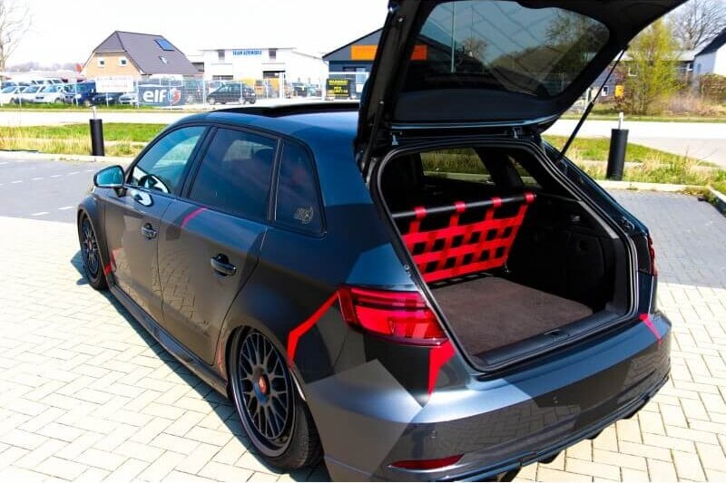 A grey Audi hatchback with its boot open, showing a Stern Performance strut bar, red net and carpet where the rear seats were
