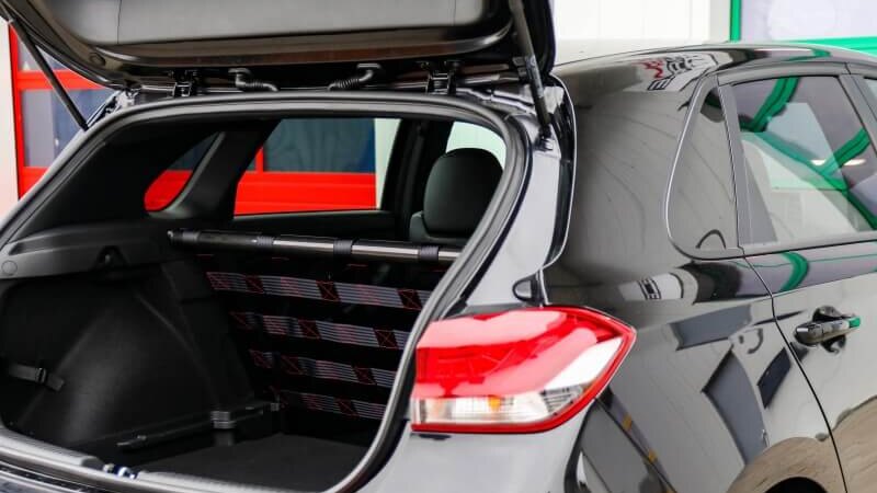 A black Hyundai i30 N with its tailgate open, showing a Stern Performance strut bar and net in place of the rear seats