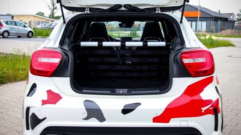 A white Mercedes A45 AMG with red and grey graphics and its tailgate open, showing a Stern Performance strut bar and black net