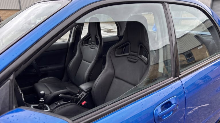 Recaro Sportster CS reclining seats fitted in a blue Subaru Impreza WRX STI, seen through the closed driver door window