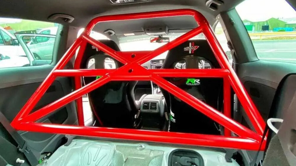 A red SW Motorsports bolt-in half cage with cross bracing behind the front seats of a Volkswagen Golf