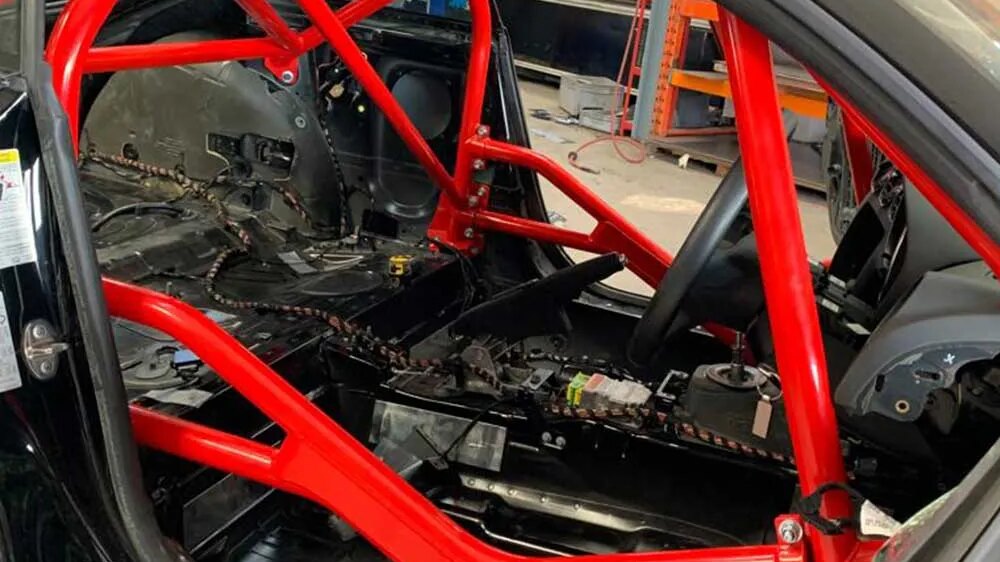 A red SW Motorsports bolt-in roll cage fitted inside a black Audi TT Mk2, seen through the driver's door