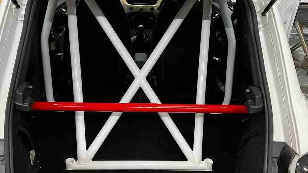 A white SW Motorsports bolt-in half cage with cross bracing and a red rear brace, seen through the open tailgate of a white Fiat 500