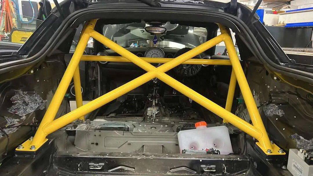 A yellow SW Motorsports bolt-in half cage with cross bracing in the back of a stripped Mini