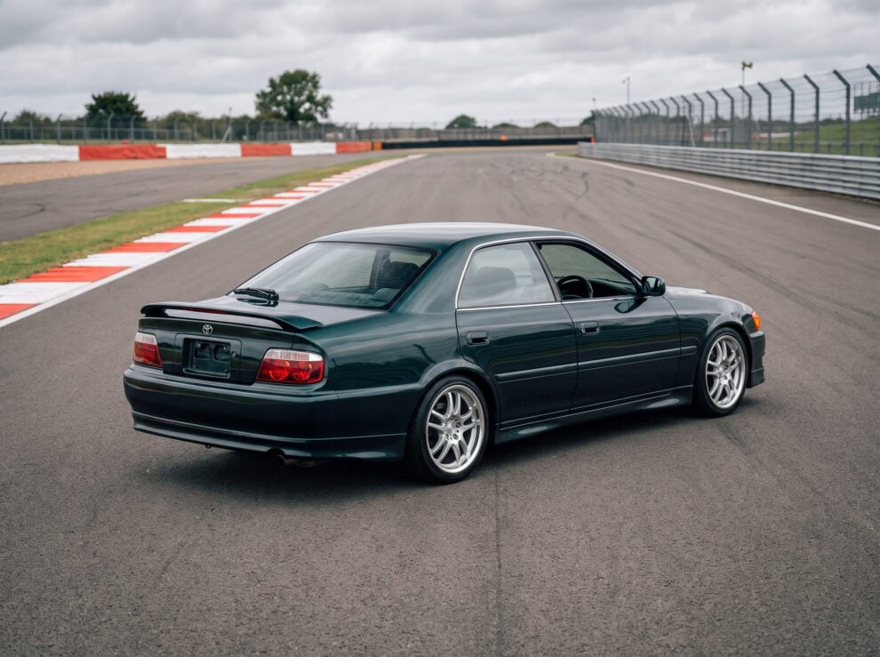 A dark green Toyota Chaser JZX100 seen from behind on a British race circuit
