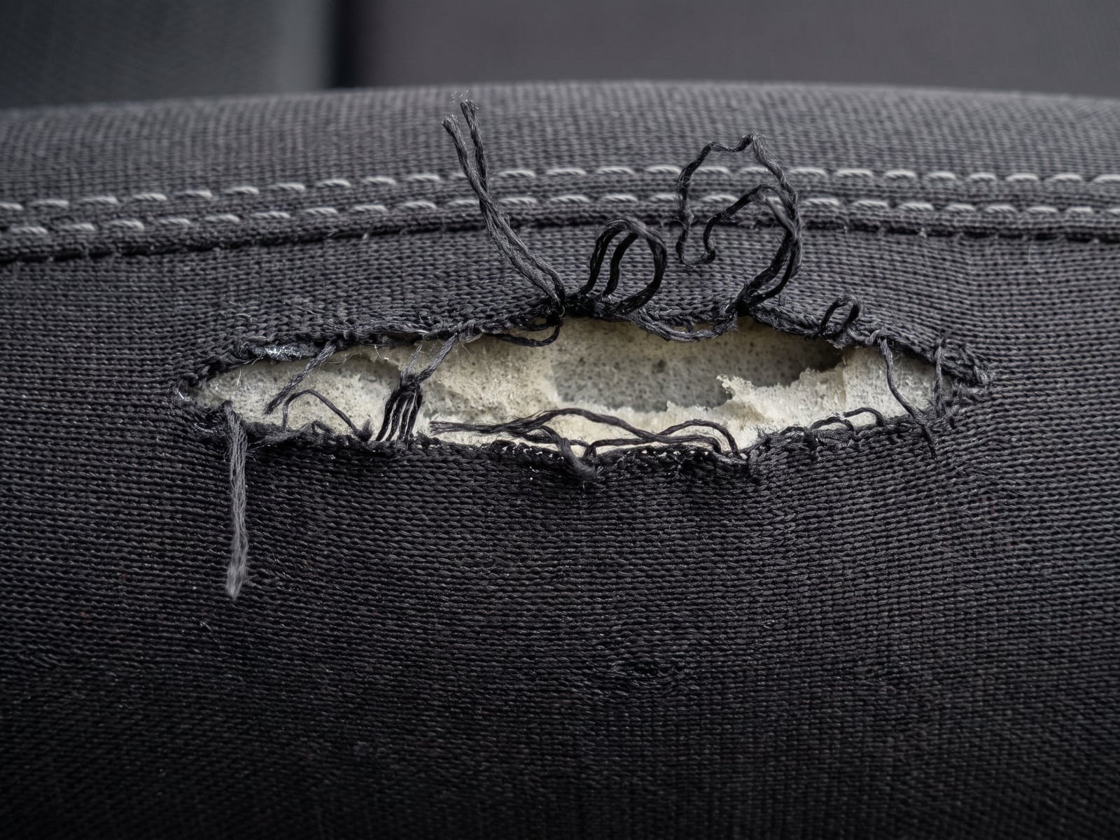 Illustration of a ragged tear in black motorsport seat fabric with broken threads of uneven length and the weave distorted