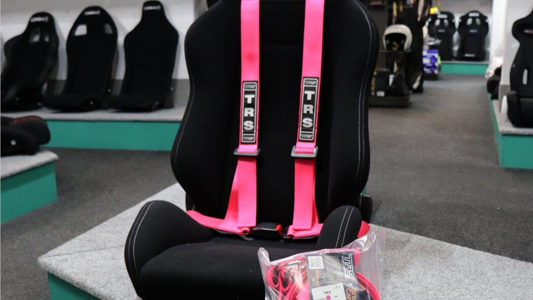 A pink TRS Clubman 4 point harness on a black sport seat on the GSM Performance showroom plinth, with a packed harness beside it