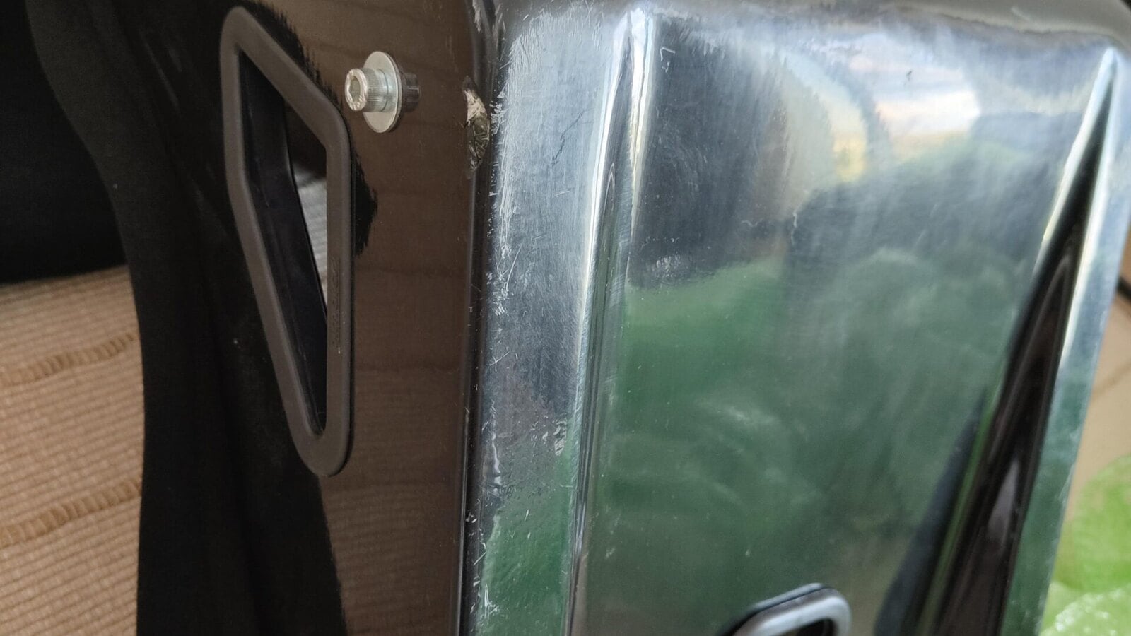 The back of a used black fibreglass bucket seat shell, covered in scratches with a chip at one edge