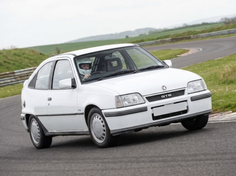 White Vauxhall Astra Mk2 GTE cornering on a British race circuit, driver in plain white helmet visible through the windscreen